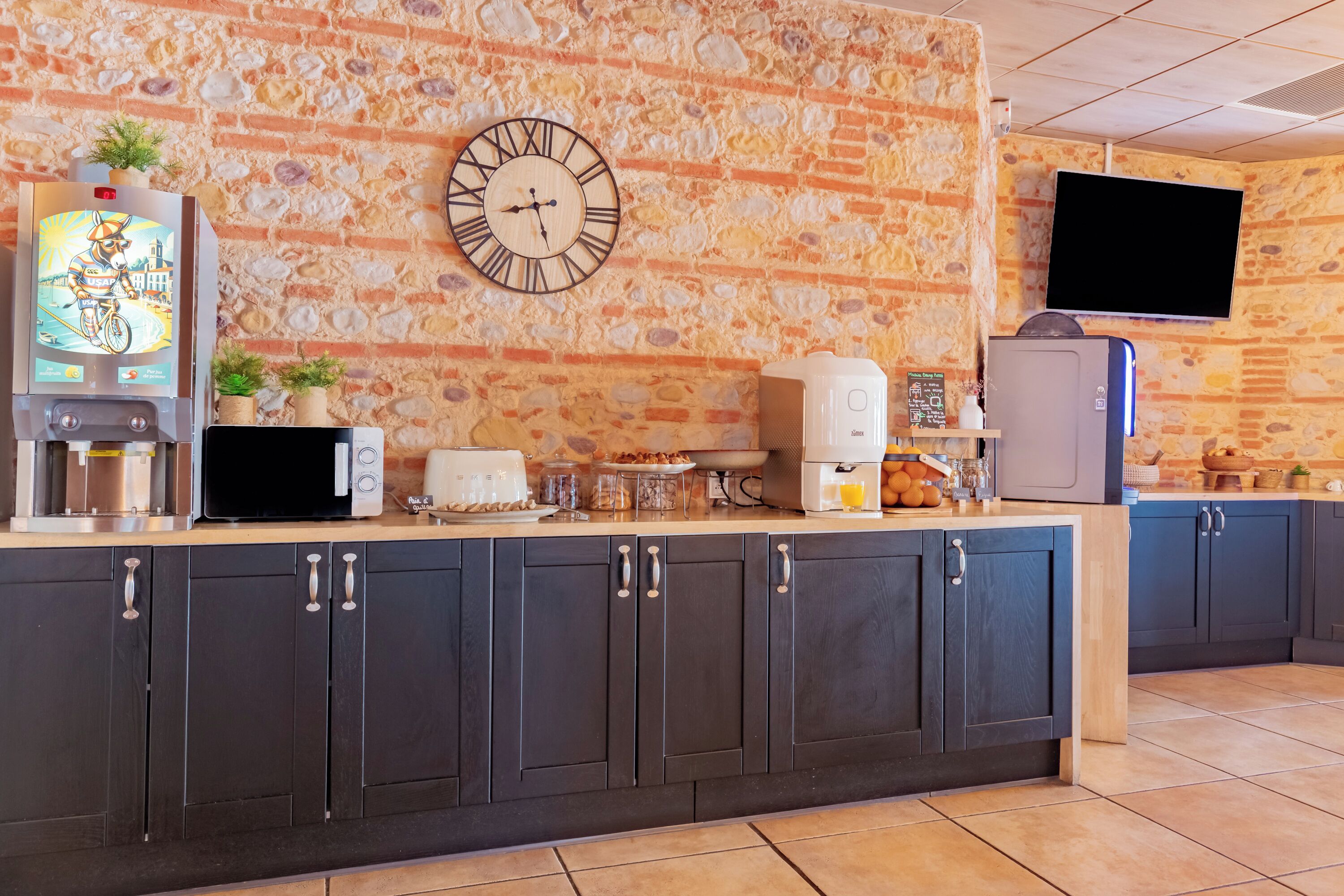 Una cocina con pared de piedra, un reloj, un televisor y diversos electrodomésticos.