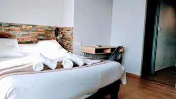 Un lit bien fait, avec du linge de lit blanc, un bureau en bois avec une chaise, et un mur décoré d’un motif en briques.