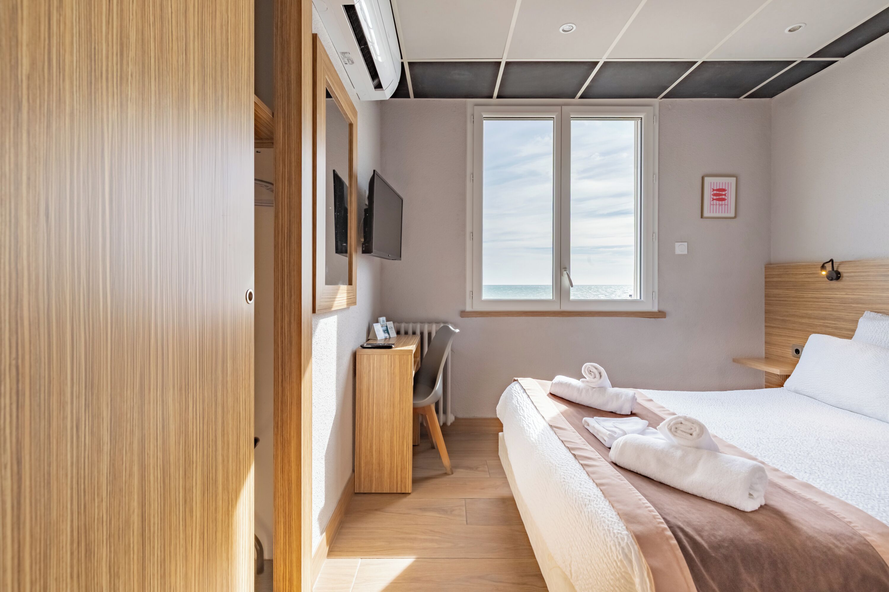 A hotel room with a bed, a desk, a chair, a TV, and a window with a view.