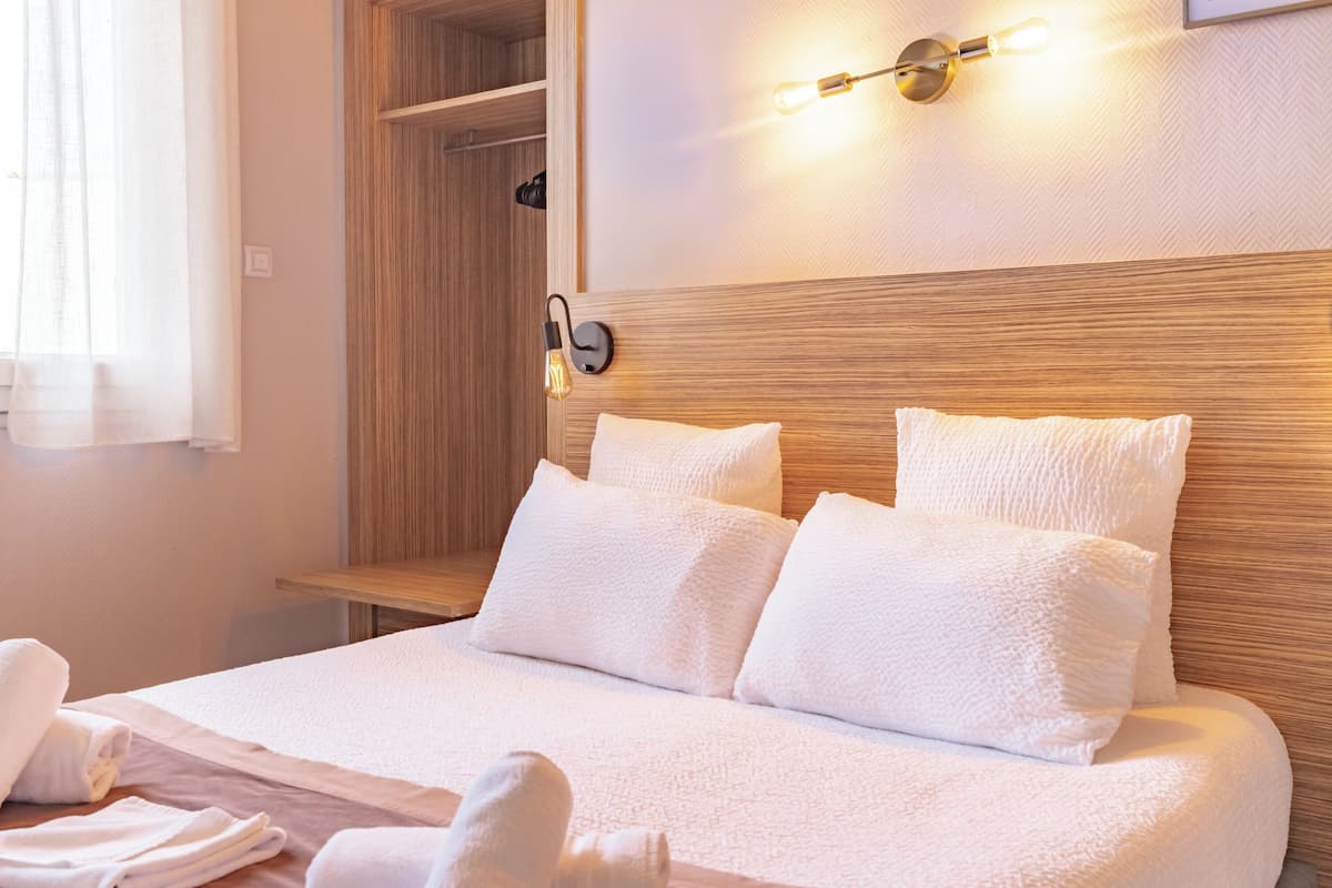 A hotel room with a wooden headboard, white bedding, and a bedside lamp.