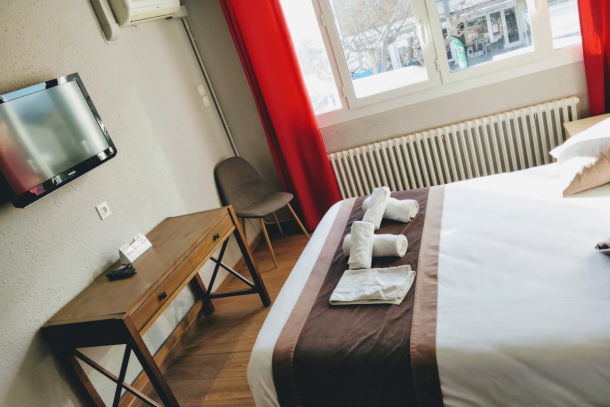 A hotel room with a bed, a TV mounted on the wall, a desk, and a chair.