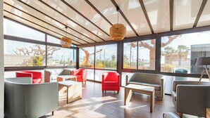 A modern lounge area with large windows, wooden flooring, and a mix of red and grey seating. - Mar I Sol (Saint-Cyprien)