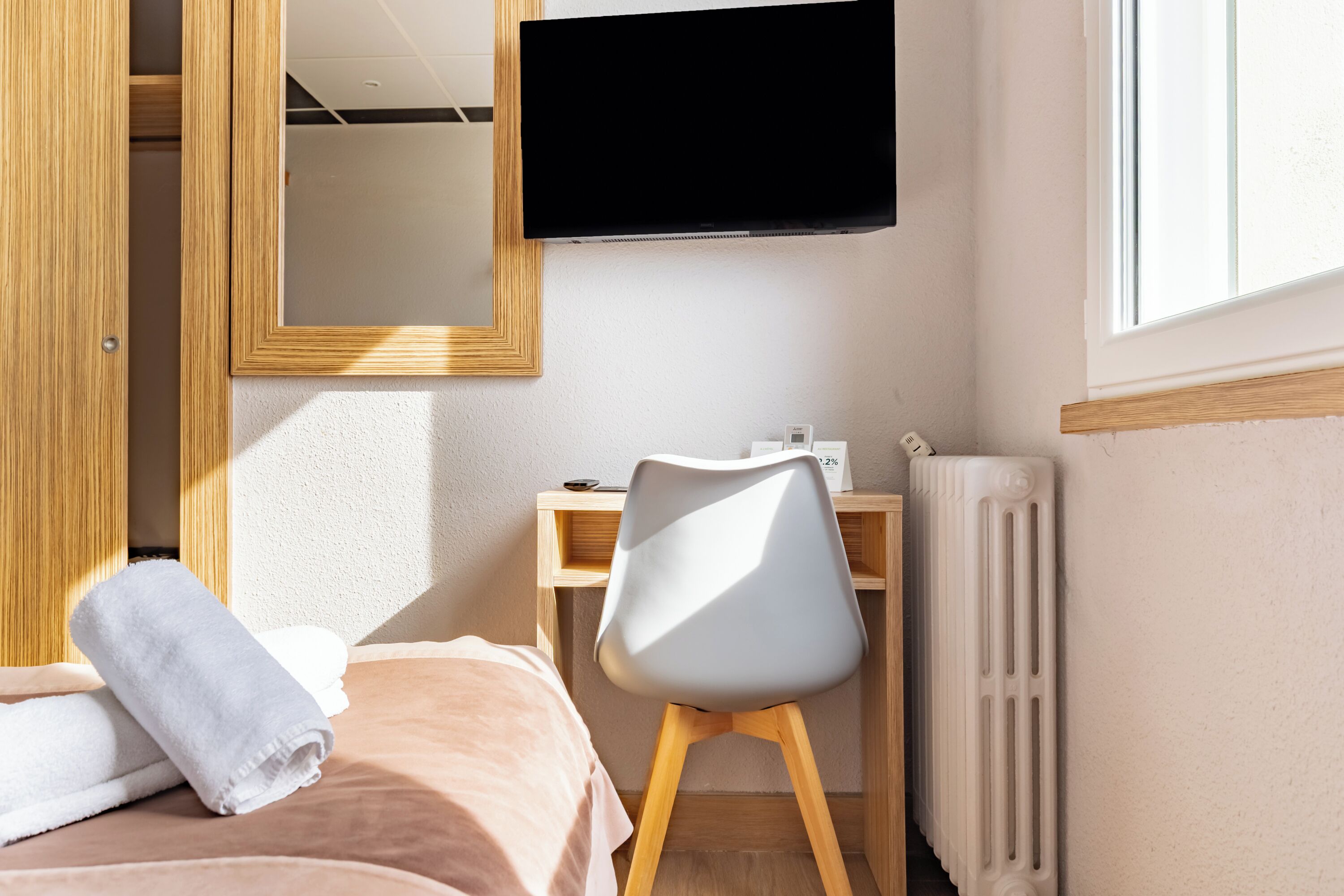 A bedroom with a bed, a desk, a chair, a TV, and a radiator.