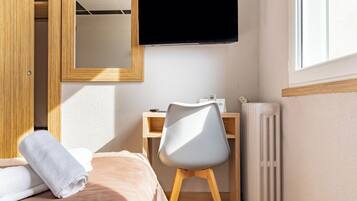 A bedroom with a bed, a desk, a chair, a TV, and a radiator.