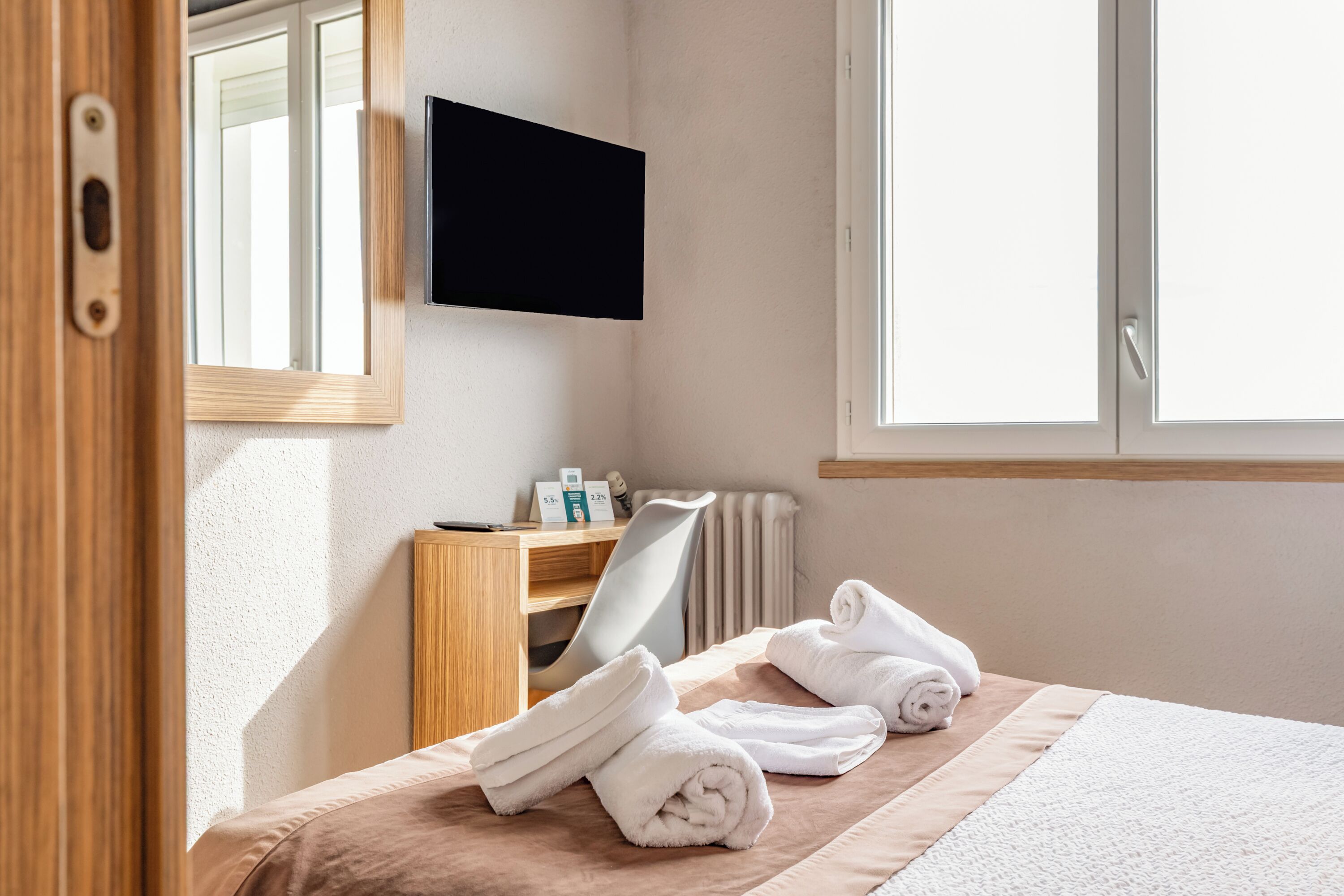 A hotel room with a bed, a desk, a chair, a TV, and a window.
