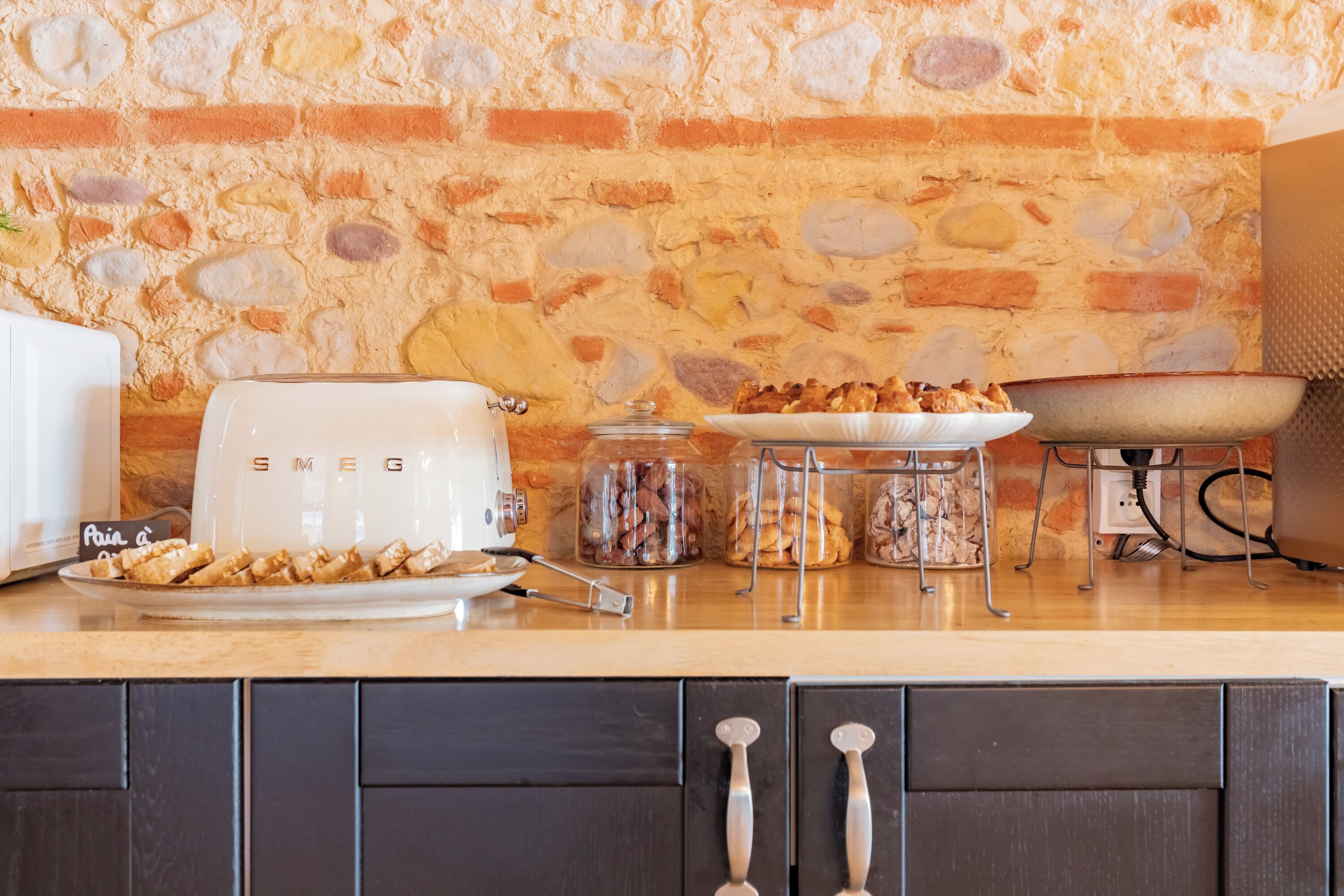 A kitchen with a stone wall, a toaster, a plate of food, jars, and a grill.