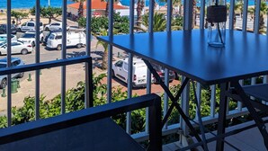 A balcony with a table and chairs, overlooking a parking area and a beach with palm trees. - Mar I Sol (Saint-Cyprien)