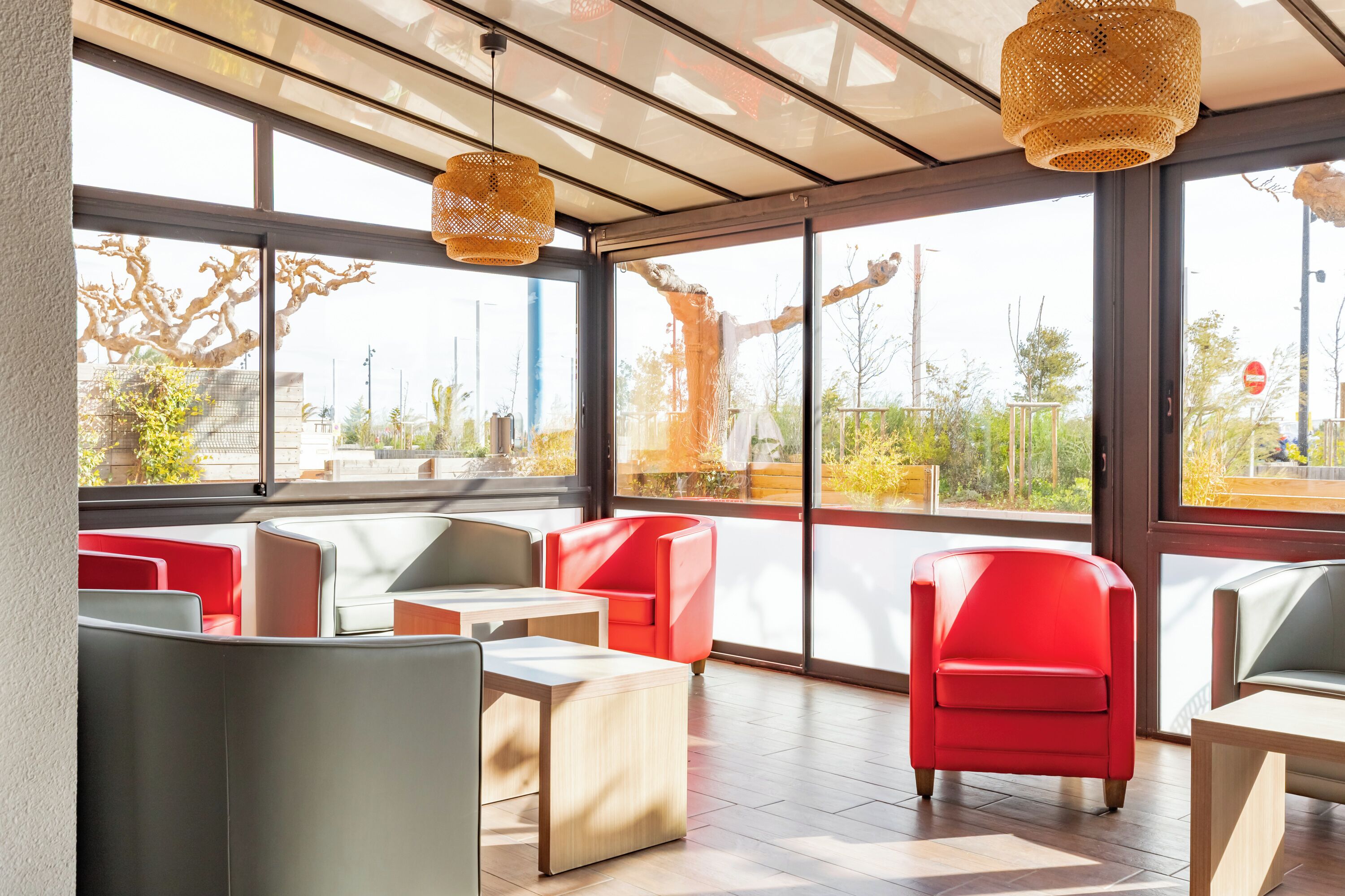 A modern interior with large windows, red and grey seating, and woven light fixtures.