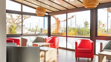A modern interior with large windows, red and grey seating, and woven light fixtures.