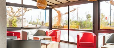 A modern interior with large windows, red and grey seating, and woven light fixtures.