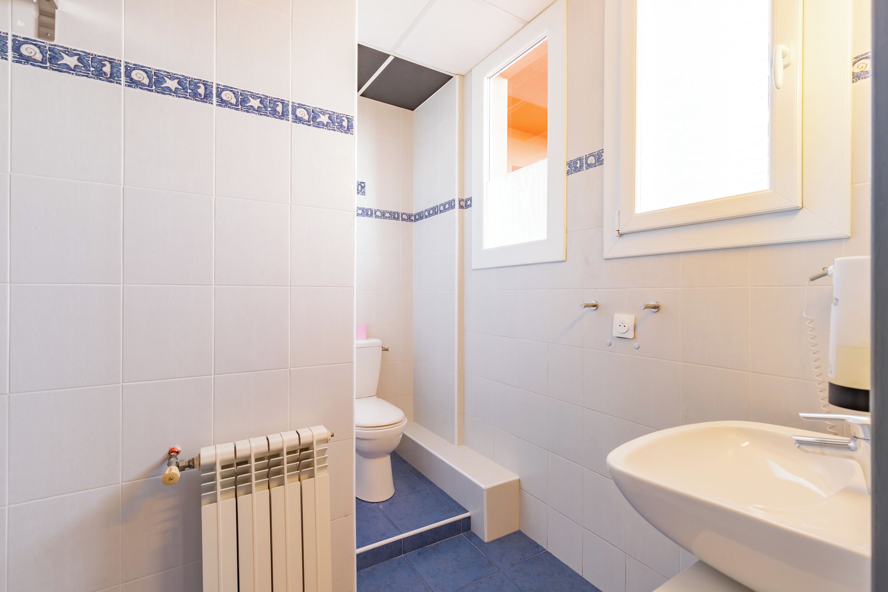 A bathroom with white tiles, a toilet, a sink, and a window.