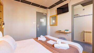 Une chambre d’hôtel équipée d’un lit, d’une télévision, d’un miroir, d’un porte-serviettes et d’un espace douche.