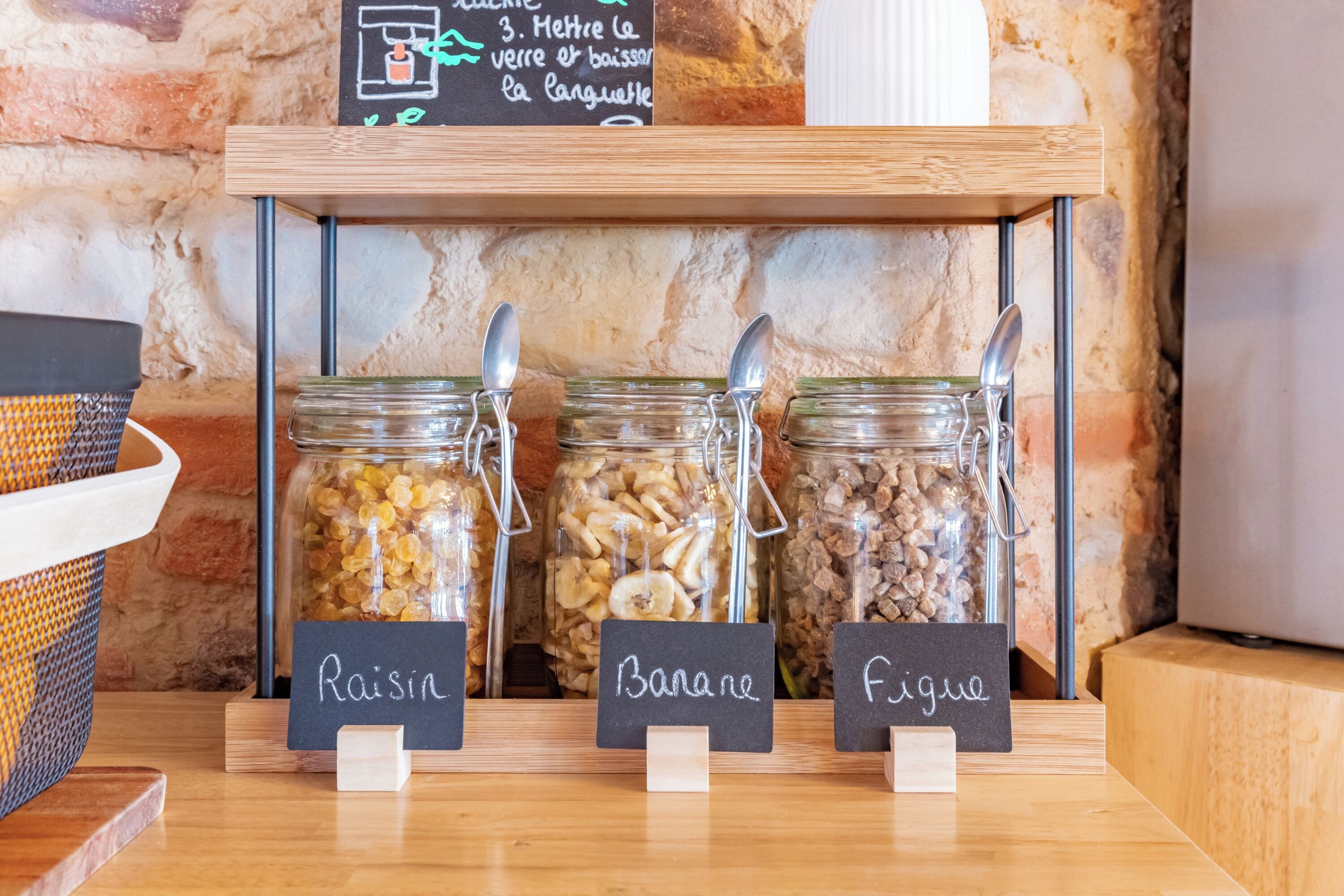 A breakfast bar with three labeled jars of granola, a chalkboard menu, and a rustic stone wall.