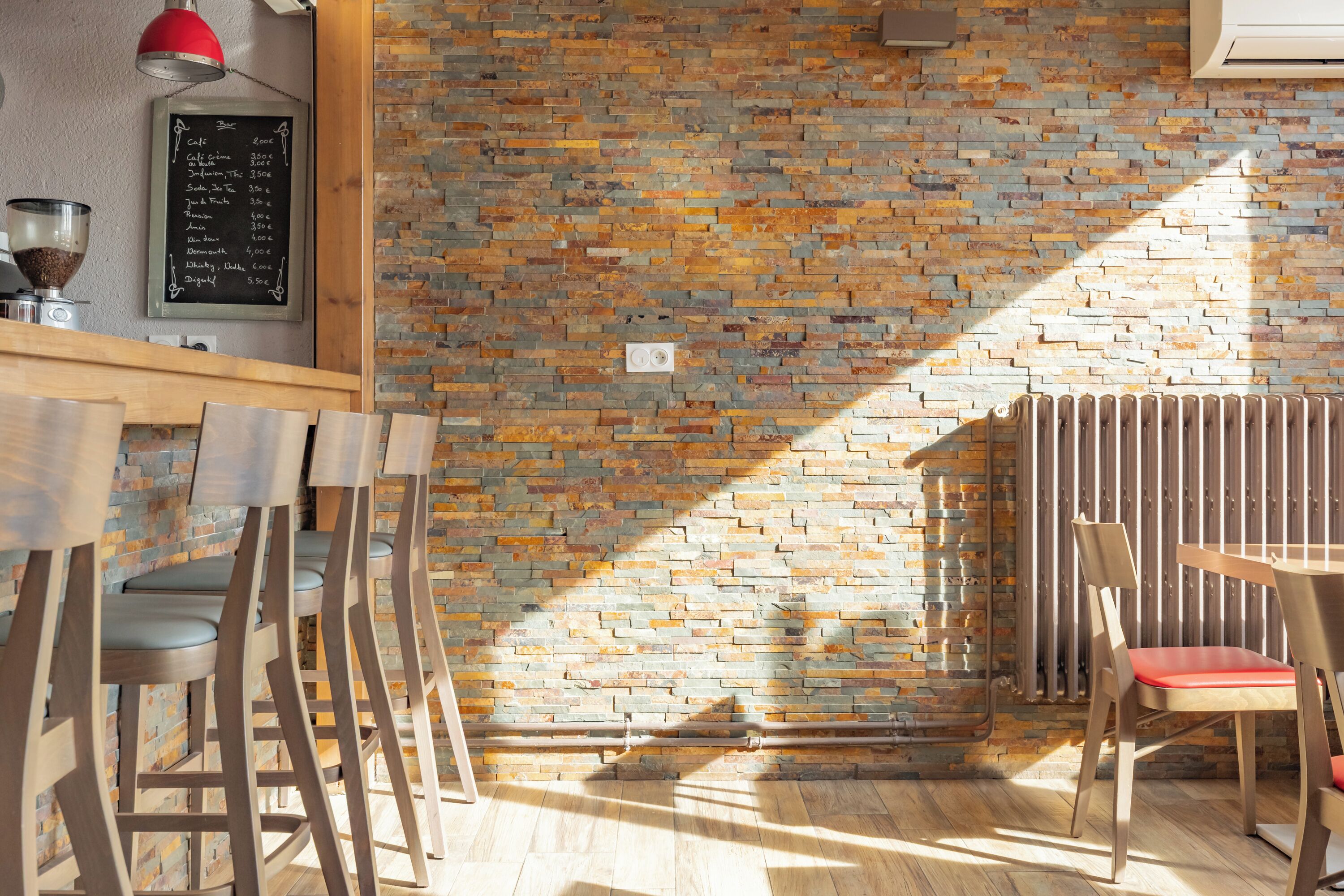 Interior de restaurante con pared de ladrillo, sillas de madera, una lámpara colgante roja y una pizarra con el menú.