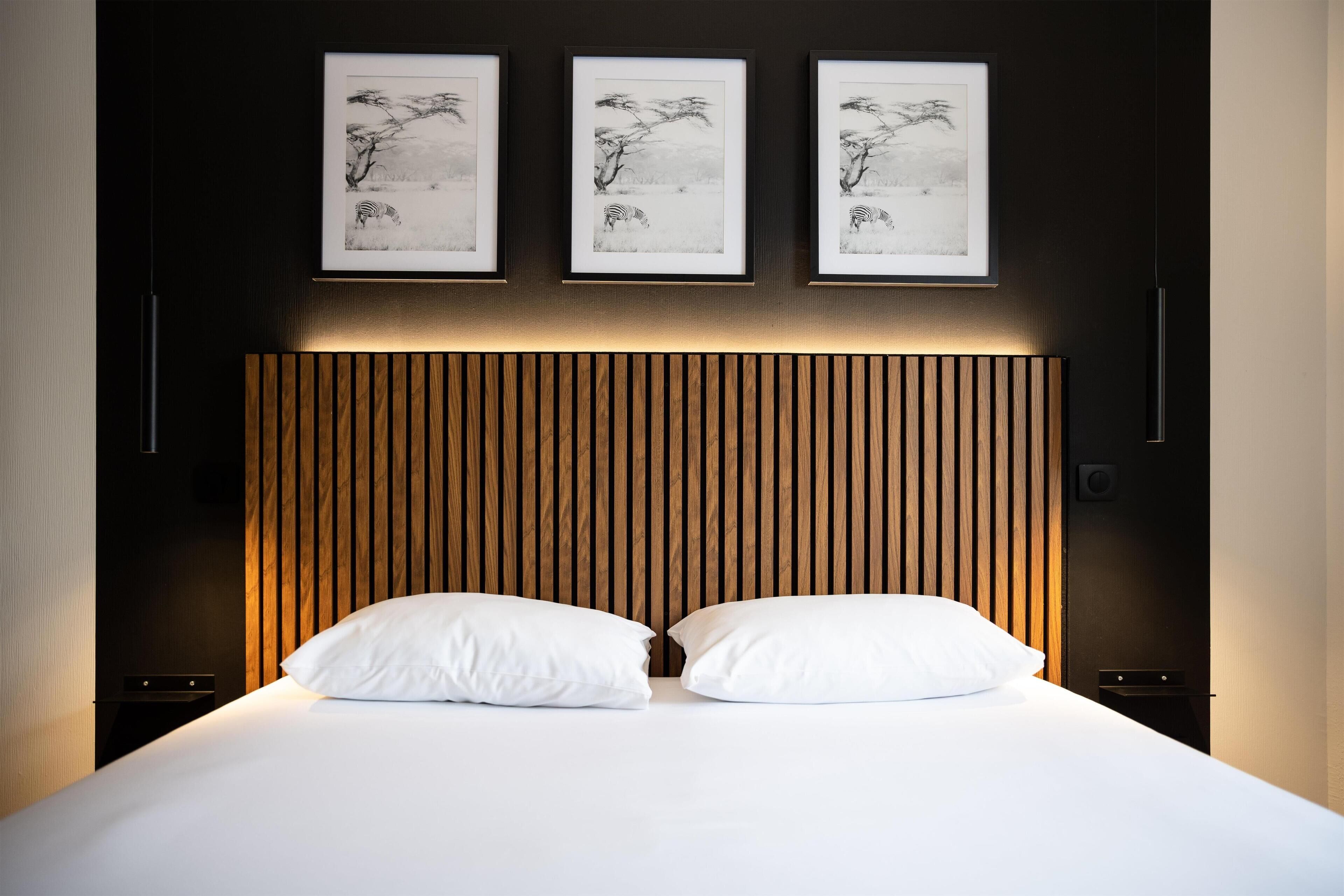 Una cama bien hecha con sábanas blancas y dos almohadas, un cabecero de listones de madera y tres fotografías en blanco y negro enmarcadas en la pared de arriba.
