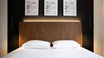 Una cama bien hecha con sábanas blancas y dos almohadas, un cabecero de listones de madera y tres fotografías en blanco y negro enmarcadas en la pared de arriba.