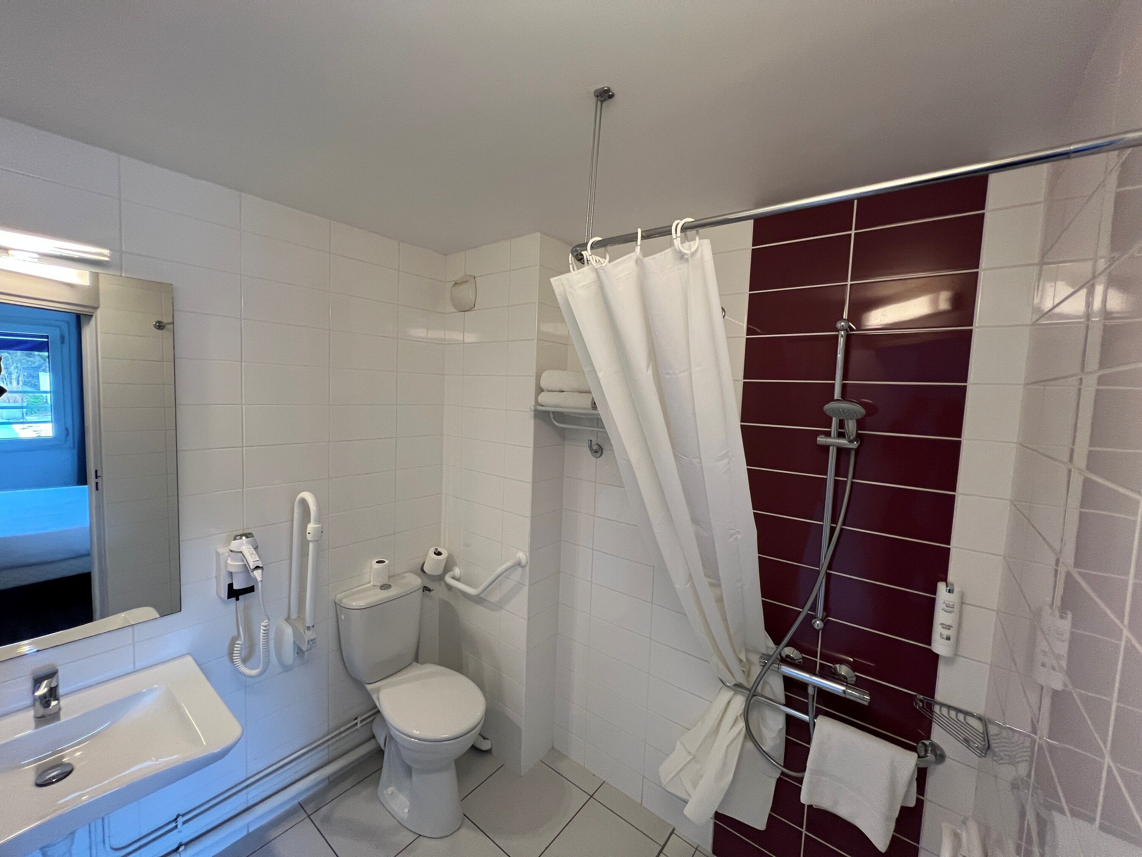 A bathroom with a white sink, toilet, and shower area with a red-tiled wall.