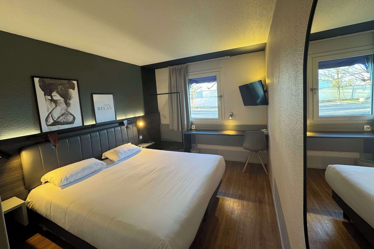 A hotel room with a large bed, a desk, a chair, a TV, and artwork on the wall.