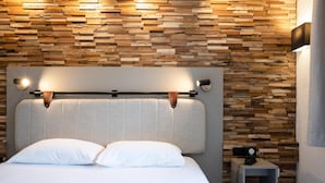A modern bedroom with a wooden wall panel, a headboard with integrated lighting, a bedside table with a phone, and a power outlet. - Tulip Inn Beaune (Beaune)