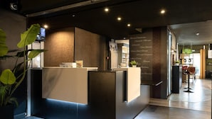 A reception desk with a modern design, a potted plant, and a menu board listing room types. - Tulip Inn Beaune (Beaune)