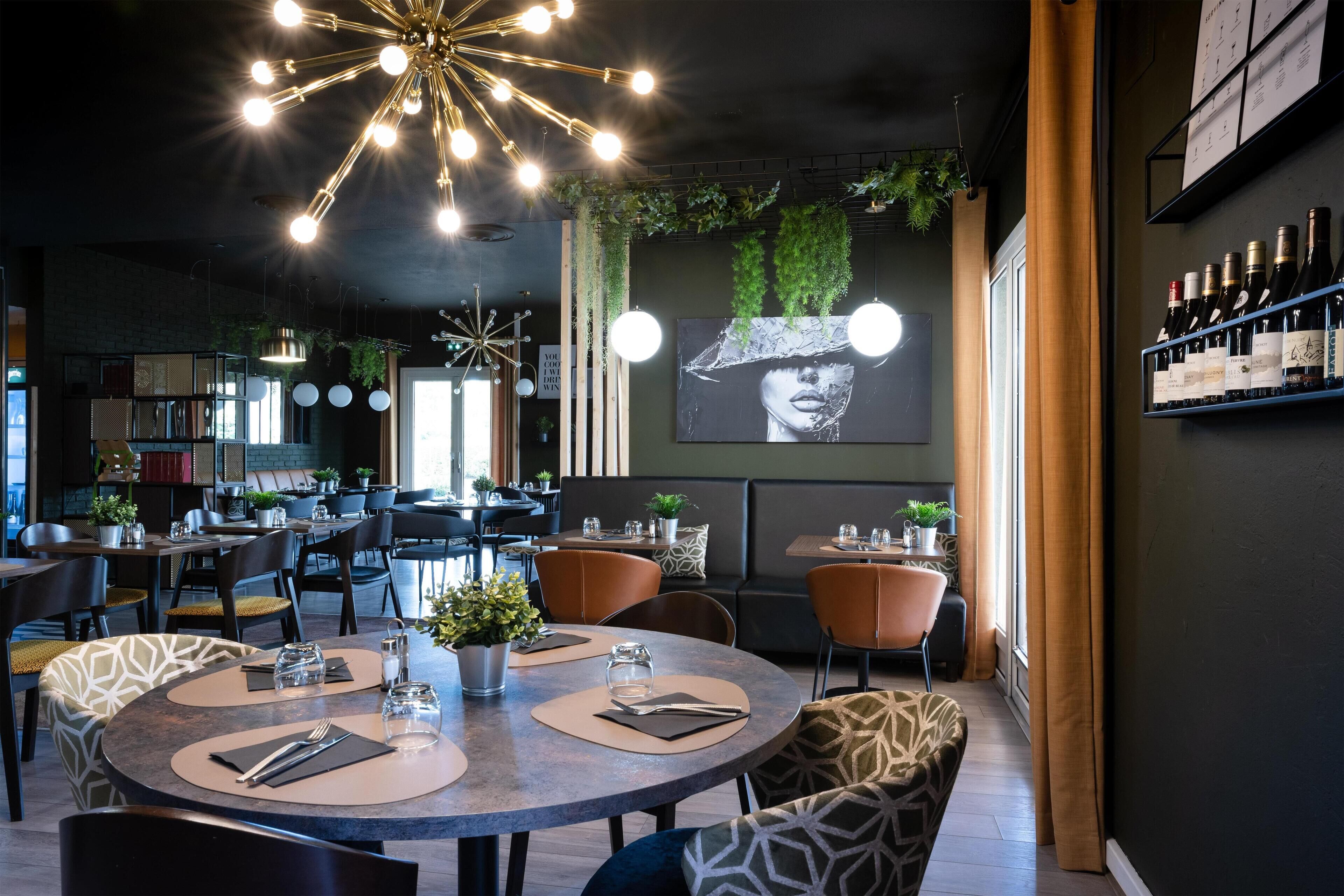 A modern restaurant with round tables, hanging lights, and a large mural on the wall.