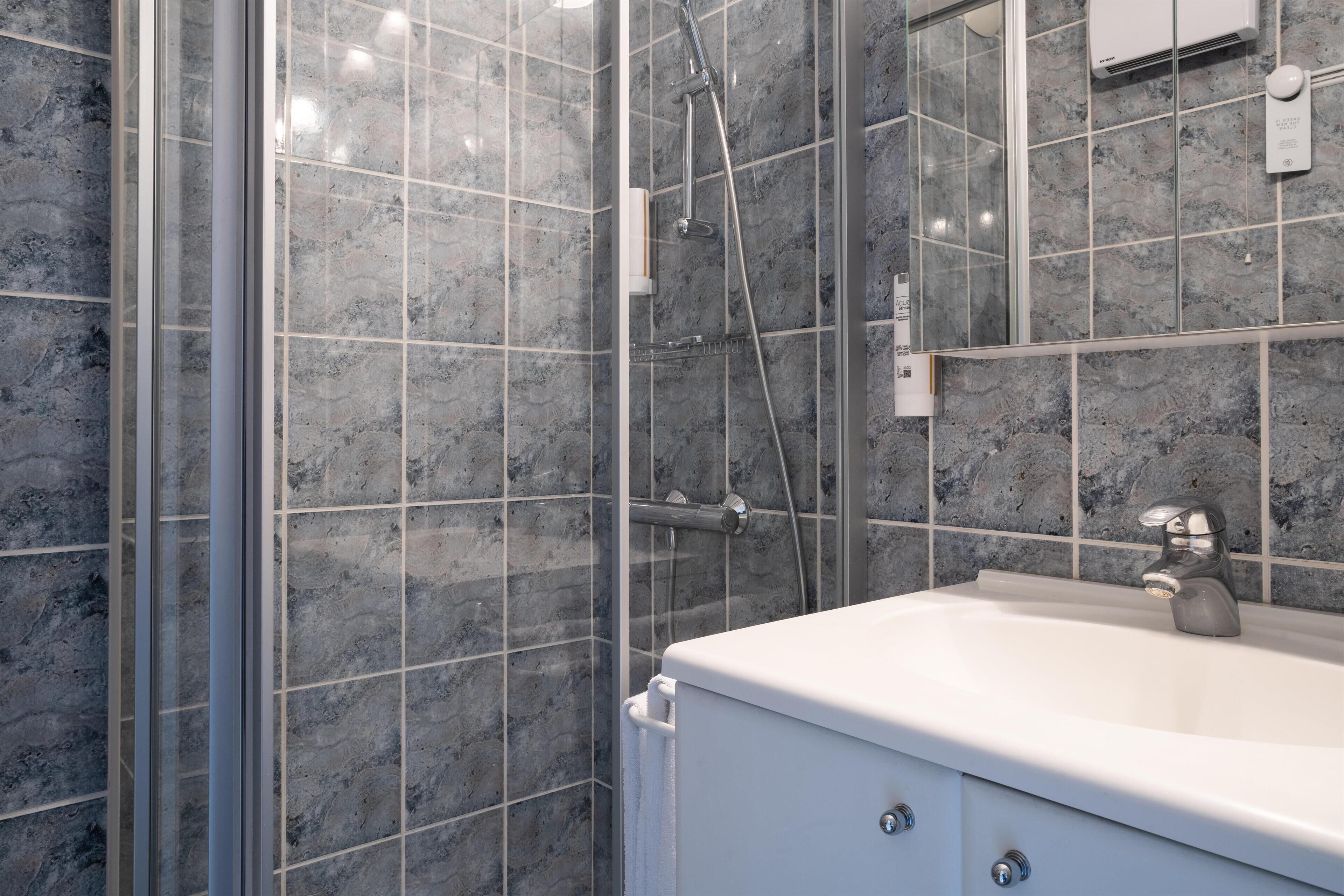 Un baño con cabina de ducha de vidrio, un lavabo blanco y un espejo.