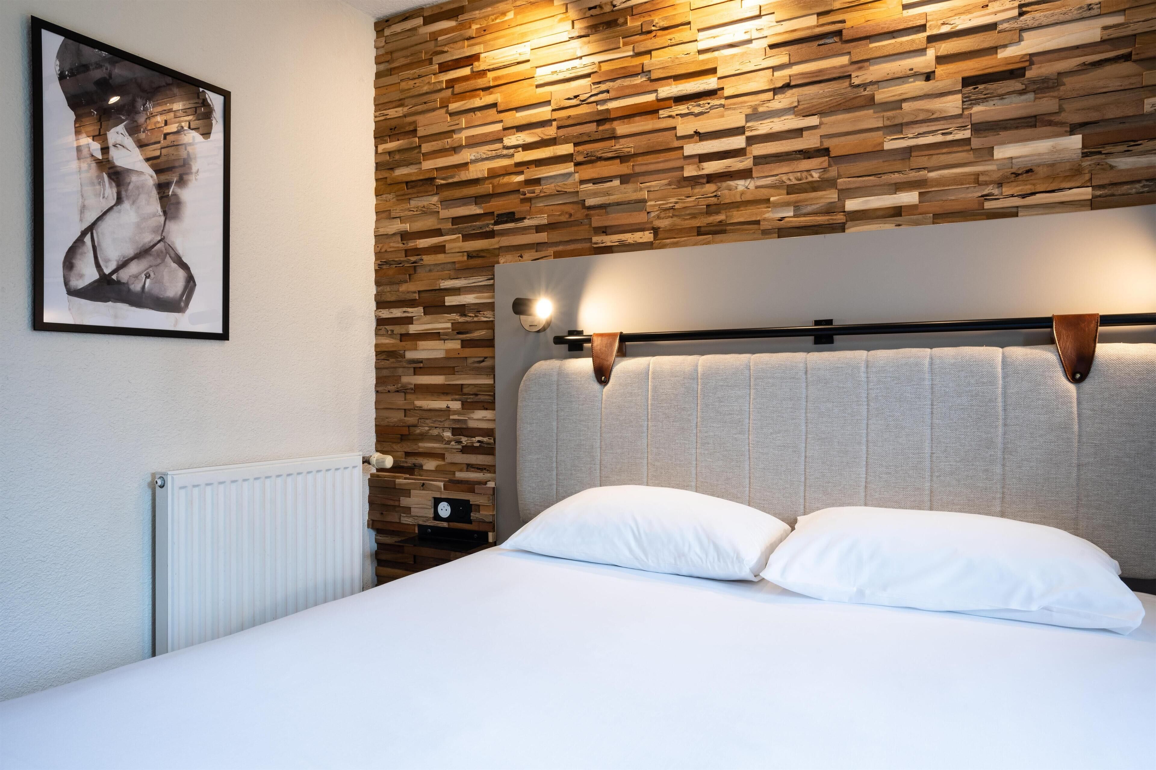 Een slaapkamer met een houten paneel, een bed met wit beddengoed en een kunstwerk in een lijst aan de muur.