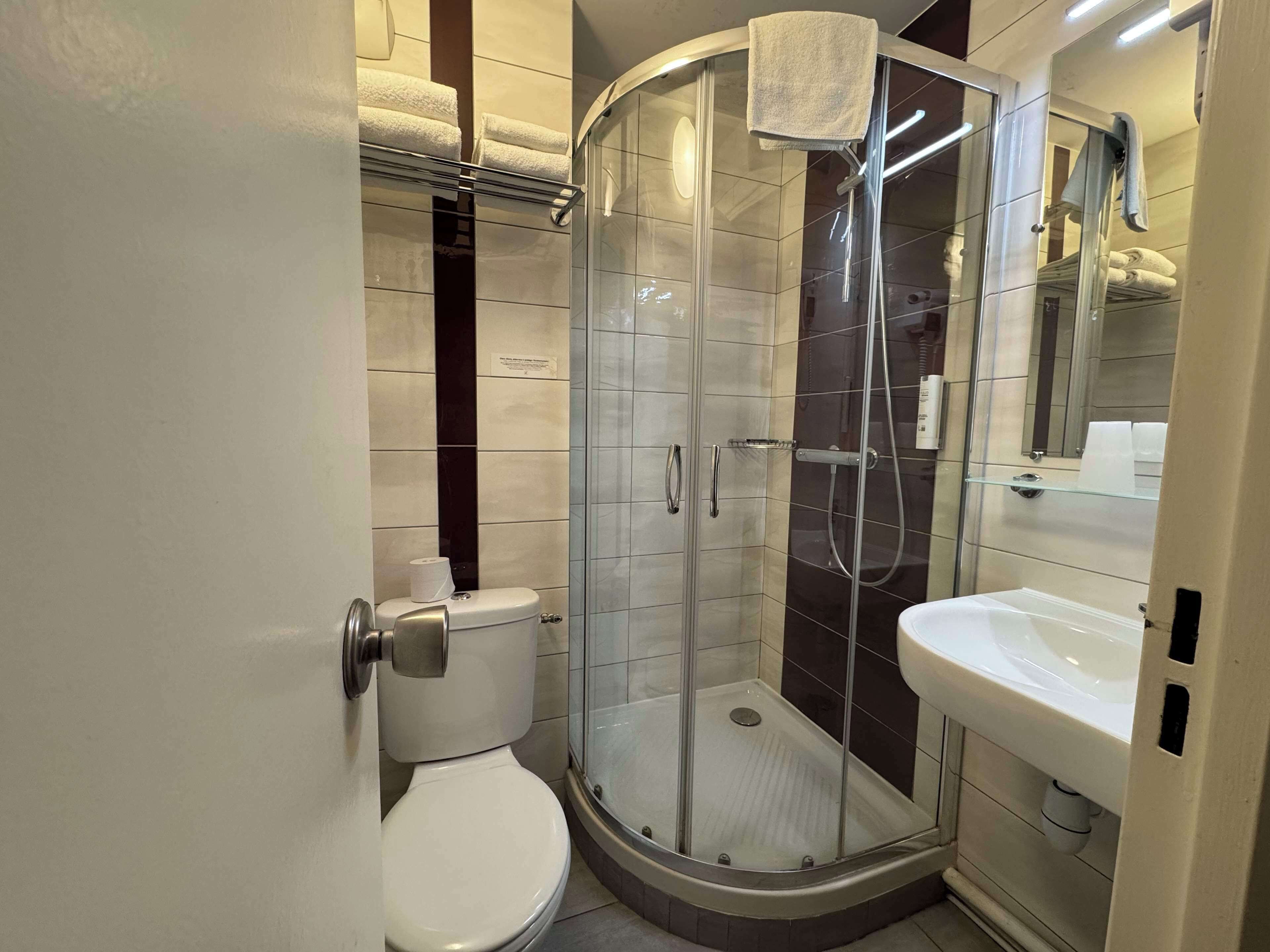 A modern bathroom with a glass-enclosed shower, a white toilet, and a sink with a mirror above it.
