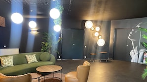 A modern lobby with a green sofa, leather chairs, a round coffee table, and a wall-mounted light fixture. - Tulip Inn Beaune (Beaune)