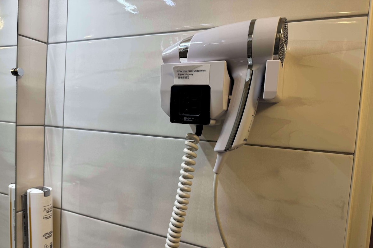 A hair dryer mounted on a tiled wall, connected to a power outlet.