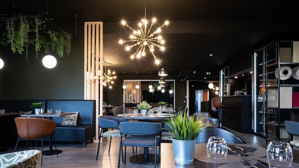 A modern restaurant with round tables, blue chairs, hanging plants, and contemporary lighting fixtures. - Tulip Inn Beaune (Beaune)