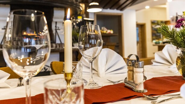 A dining table set with wine glasses, a candle, salt and pepper shakers, and a vase with flowers. - Alpenhotel Ensmann (Goestling an der Ybbs)