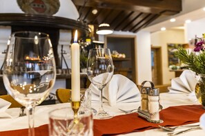 A dining table set with wine glasses, a candle, salt and pepper shakers, and a vase with flowers. - Alpenhotel Ensmann (Goestling an der Ybbs)