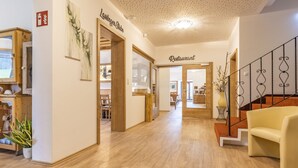 A hotel lobby with a wooden floor, a staircase with black railings, and a yellow sofa. - Alpenhotel Ensmann (Goestling an der Ybbs)