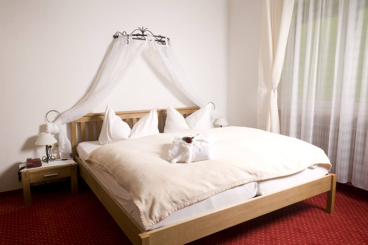 A neatly made bed with a canopy, a bedside table with a lamp, and a telephone.