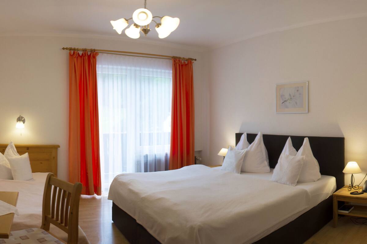A hotel room with a large bed, a desk with a chair, a bedside table with a lamp, and a television on the wall.