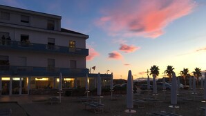 A beachside hotel with multiple lounge chairs and umbrellas, a pool area, and a building with balconies overlooking the beach. - Hotel Strand (Montenero di Bisaccia)