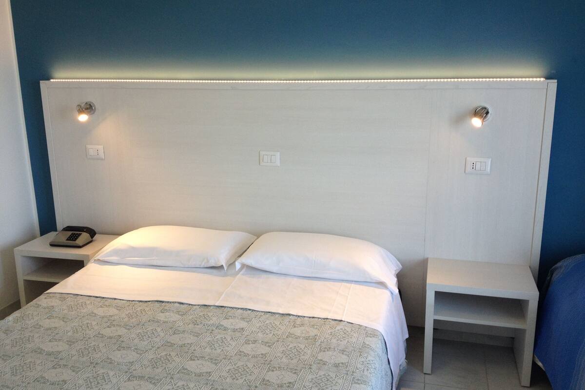 A hotel room with a bed, two bedside tables, and a nightstand with a phone.