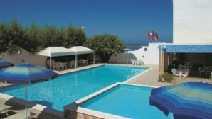 A swimming pool with lounge chairs and umbrellas, a covered seating area, and a view of the sea. - Hotel Strand (Montenero di Bisaccia)
