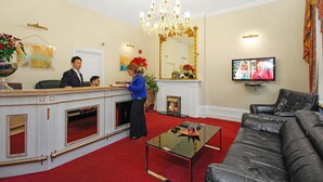 Een receptiegedeelte met een balie, een kroonluchter, een open haard, een televisie en een leren bank.