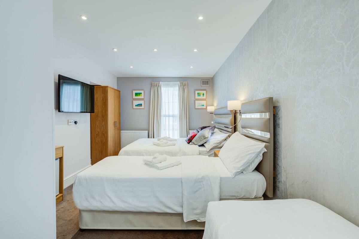 Een hotelkamer met twee bedden, een flatscreen televisie aan de muur, een nachtkastje en een raam met gordijnen.