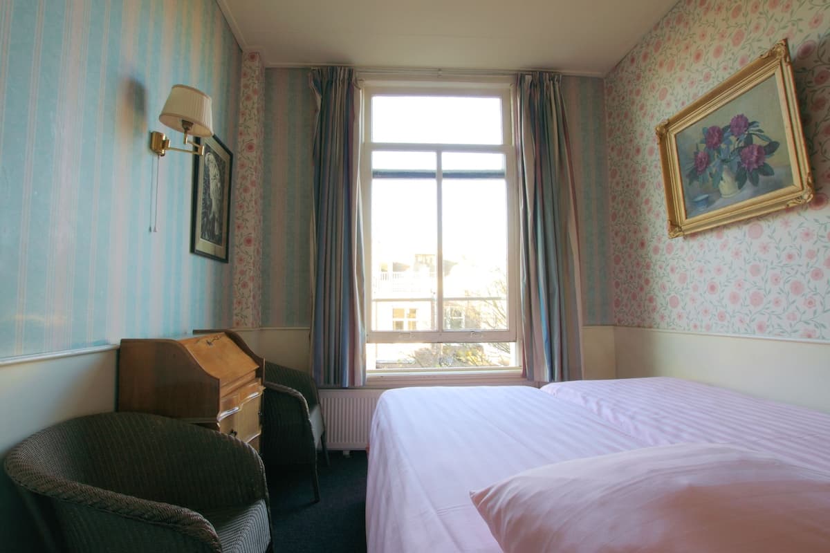 A bedroom with a bed, a dresser, a chair, a window with curtains, and a wall-mounted picture.