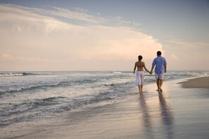 Un couple se promène sur une plage, avec des vagues en arrière-plan.