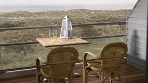 Ein Balkon mit Korbstühlen und einem Tisch, mit Blick auf eine Küstenlandschaft.