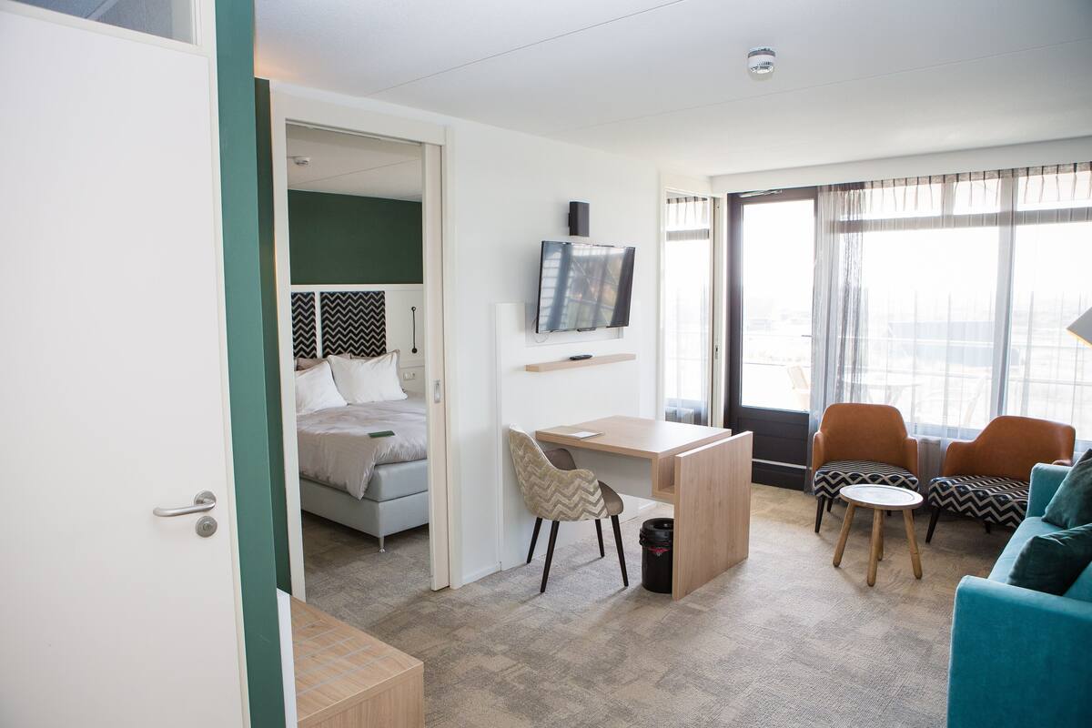 Ein modernes Hotelzimmer mit Bett, Schreibtisch, Fernseher, zwei Sesseln und einer Couch.