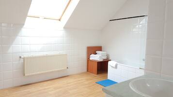 Un baño moderno con baldosas blancas, suelo de madera, tragaluz, radiador, estante de madera con toallas y bañera.