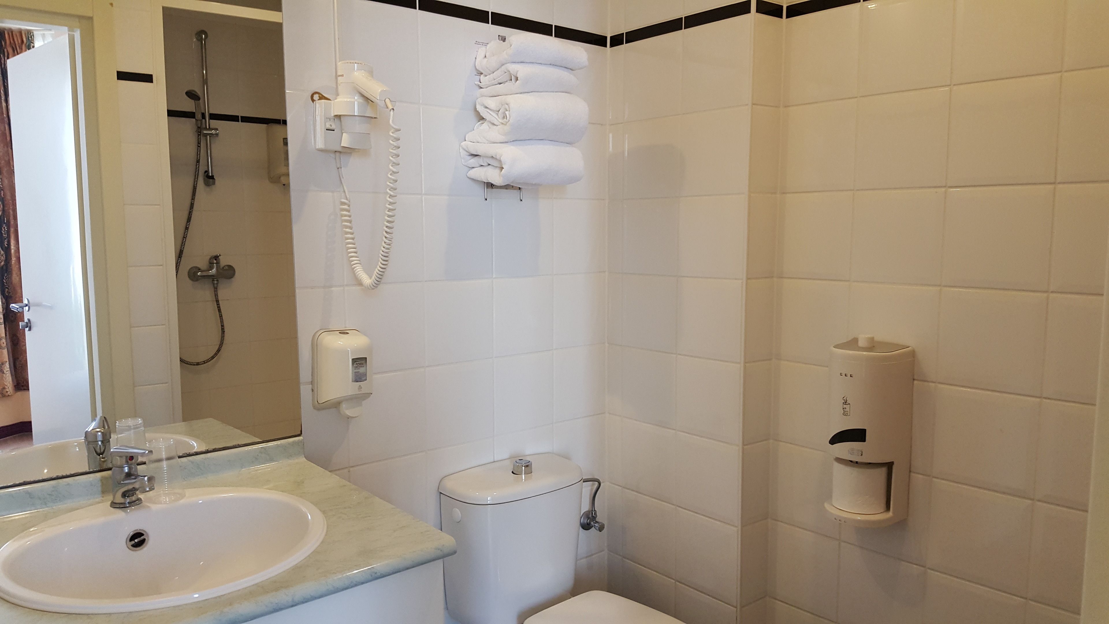 Un baño con lavamanos, inodoro, dispensador de toallas y ducha con cabezal de ducha de mano.