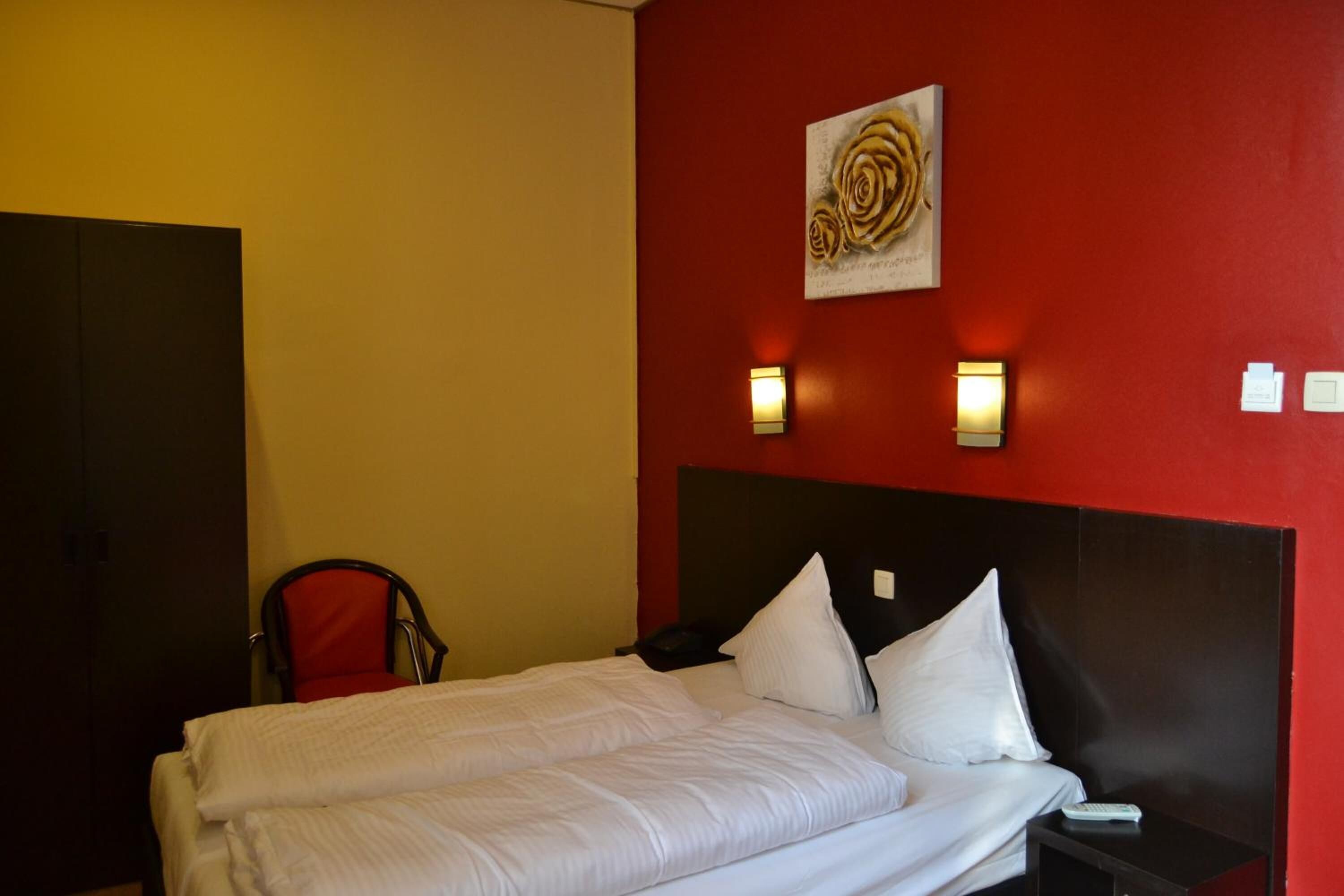 Una habitación de hotel con una cama, una silla y una pared roja con un cuadro.