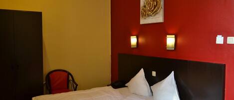 Una habitación de hotel con una cama, una silla y una pared roja con un cuadro.