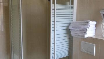A bathroom with a glass-enclosed shower, a toilet, and a towel rack with folded towels.
